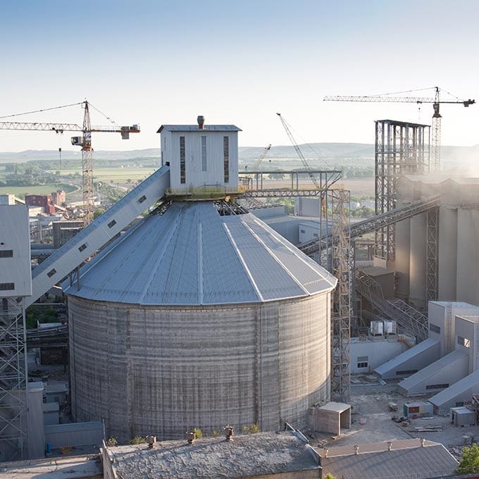 Large industrial facility with a cylindrical silo and metal structures, surrounded by cranes and construction equipment under a clear sky.