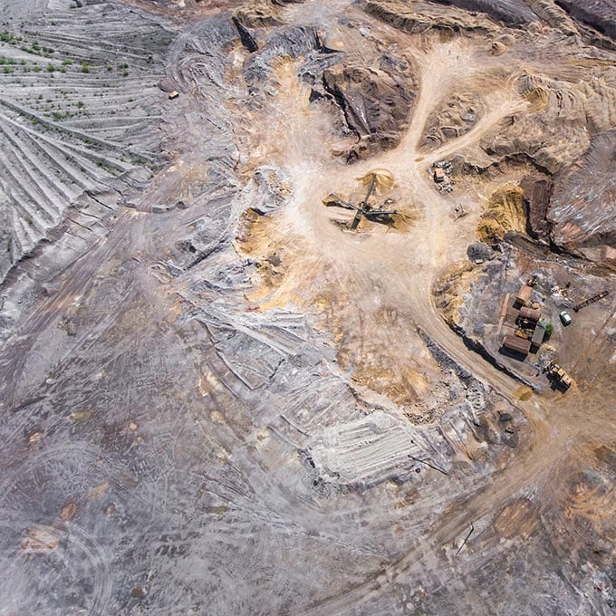 Aerial view of an open-pit mining site with exposed earth, machinery, and tracks visible across the barren landscape.