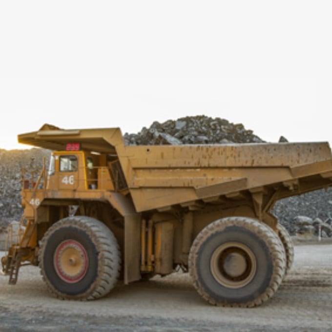 Large yellow mining dump truck numbered 46 is parked on a dirt road with a pile of rocks in the background under a clear sky.