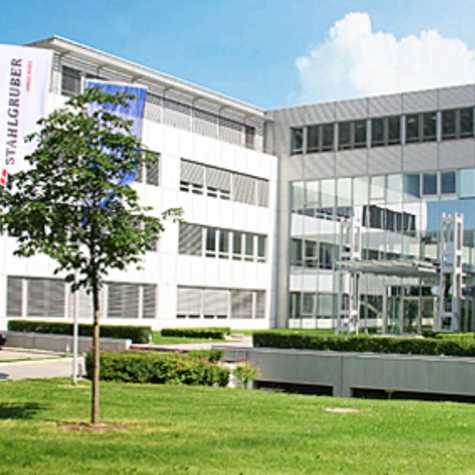 Modern office building with large windows, a tree and green lawn in the foreground, and a banner on the left side of the building.