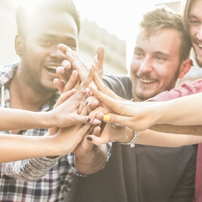 A group of people standing close together, smiling, and joining hands in the center for a high-five gesture.